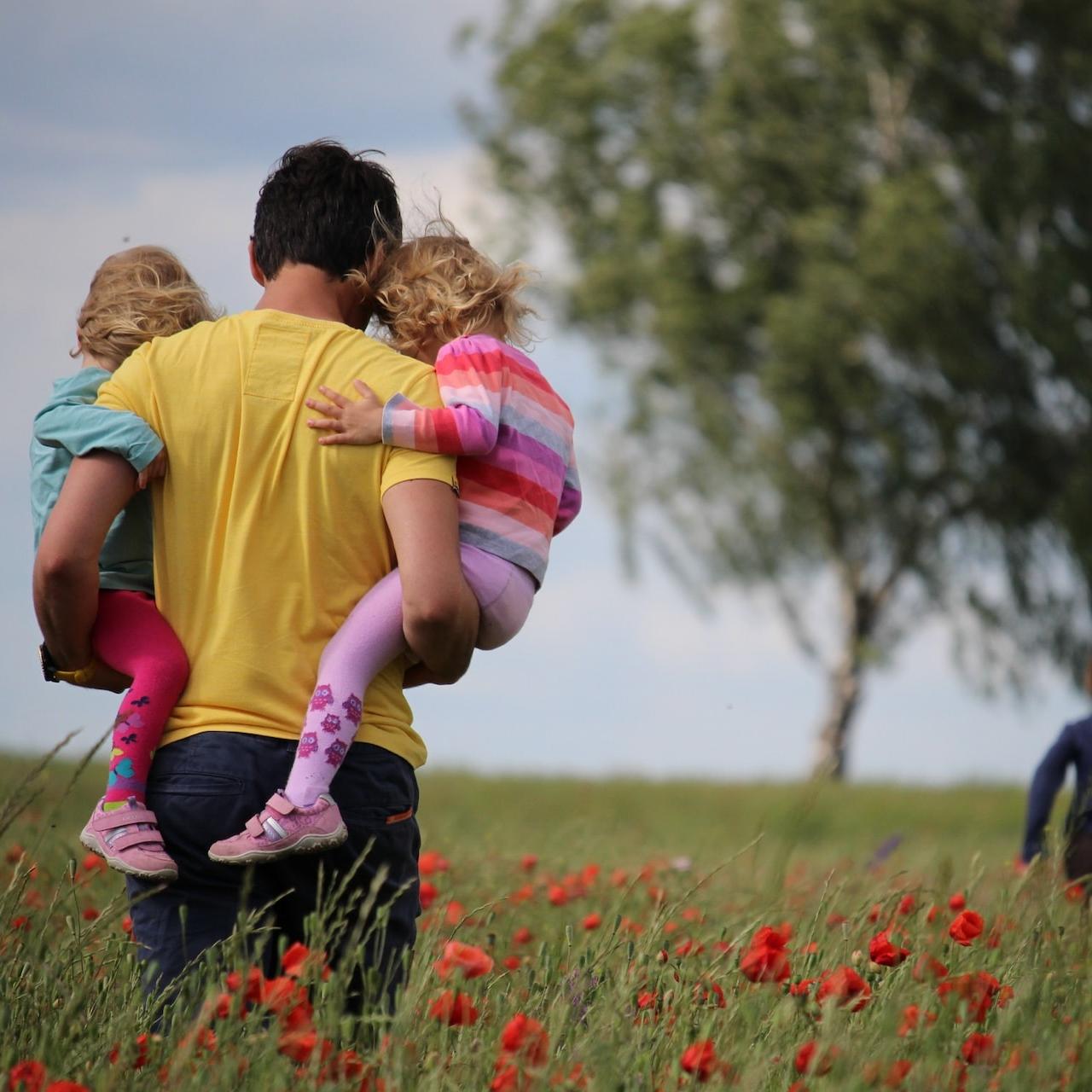 man carrying to girls on field of red petaled flower