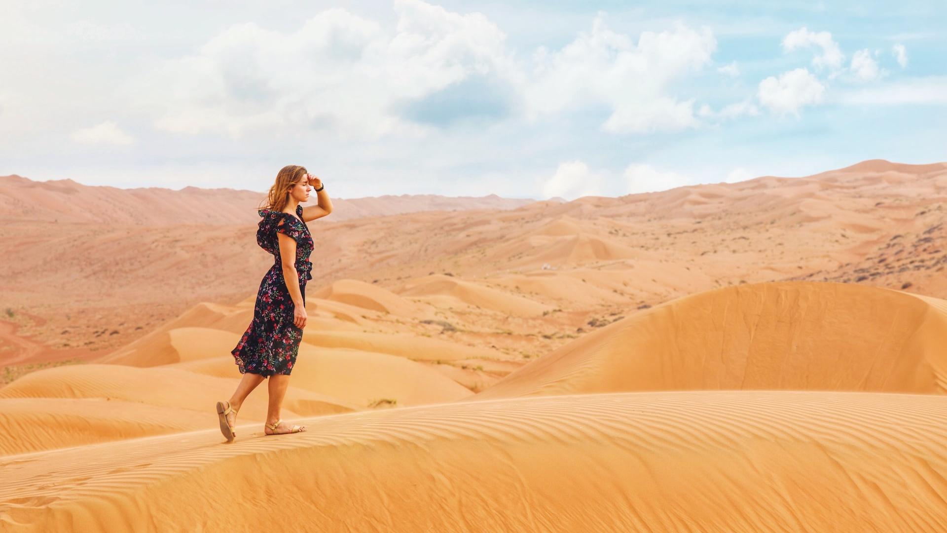 woman walking on sand dunes during daytime