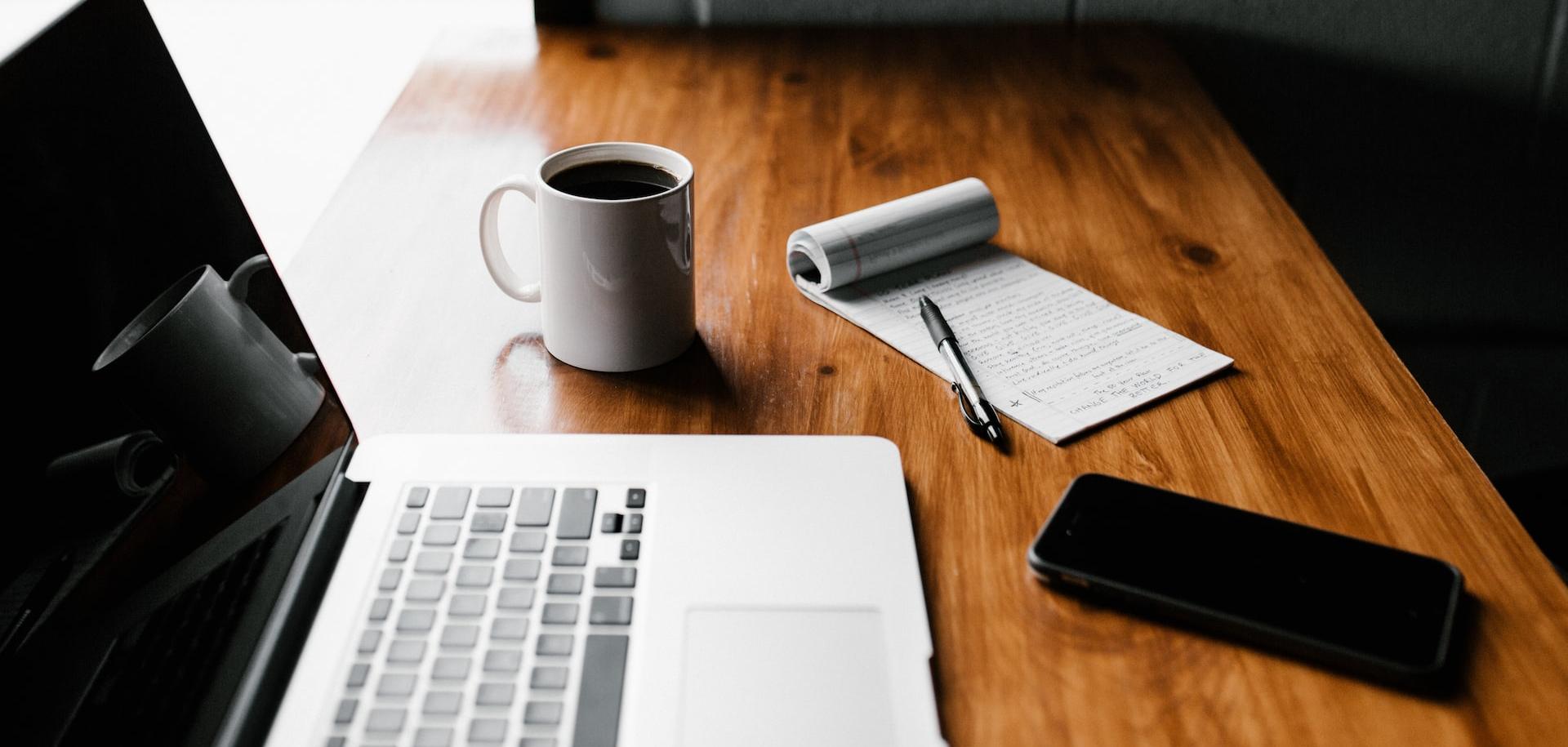 MacBook Pro, white ceramic mug,and black smartphone on table